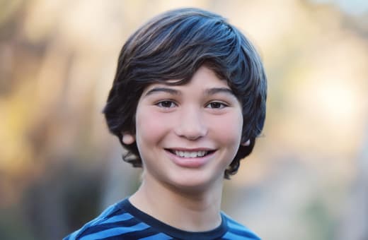 A young boy smiling while standing outdoors.