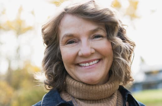 An older woman smiling while standing outdoors. An older woman smiling while standing outdoors.