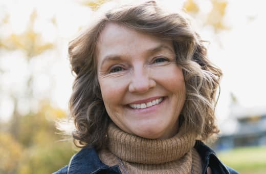 An older woman smiling while standing outdoors.