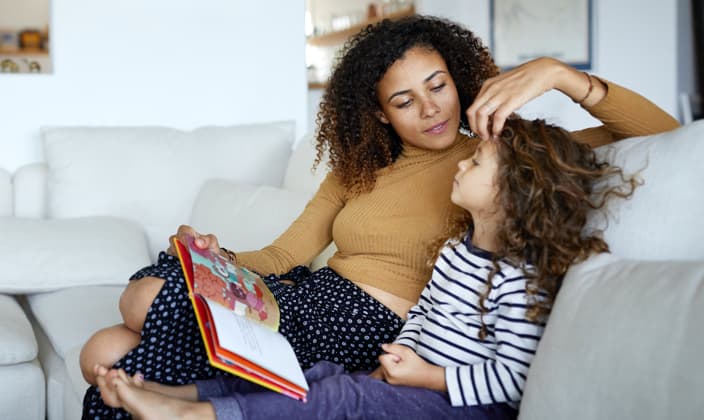 Mother reading a book to her daughter while stroking her hair.